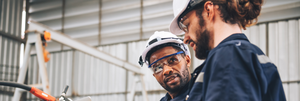 Two workers in safety gear discussing paperwork.